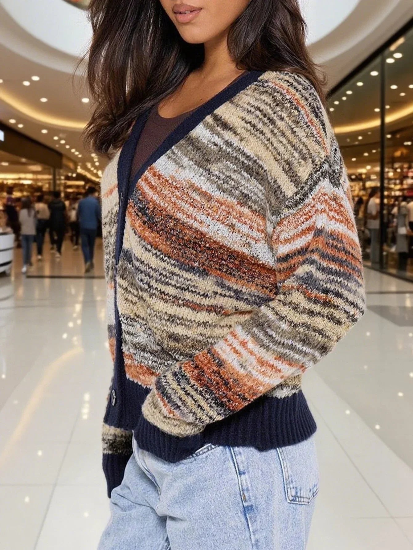 Side view of a woman wearing a multicolored striped knit cardigan with a V-neck and button-up front, paired with light-wash jeans.