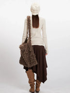 Model wearing a cream ribbed turtleneck sweater, brown asymmetrical hem skirt, cream belt, brown boots, cream knit beanie, and a brown faux fur shoulder bag, back view.
