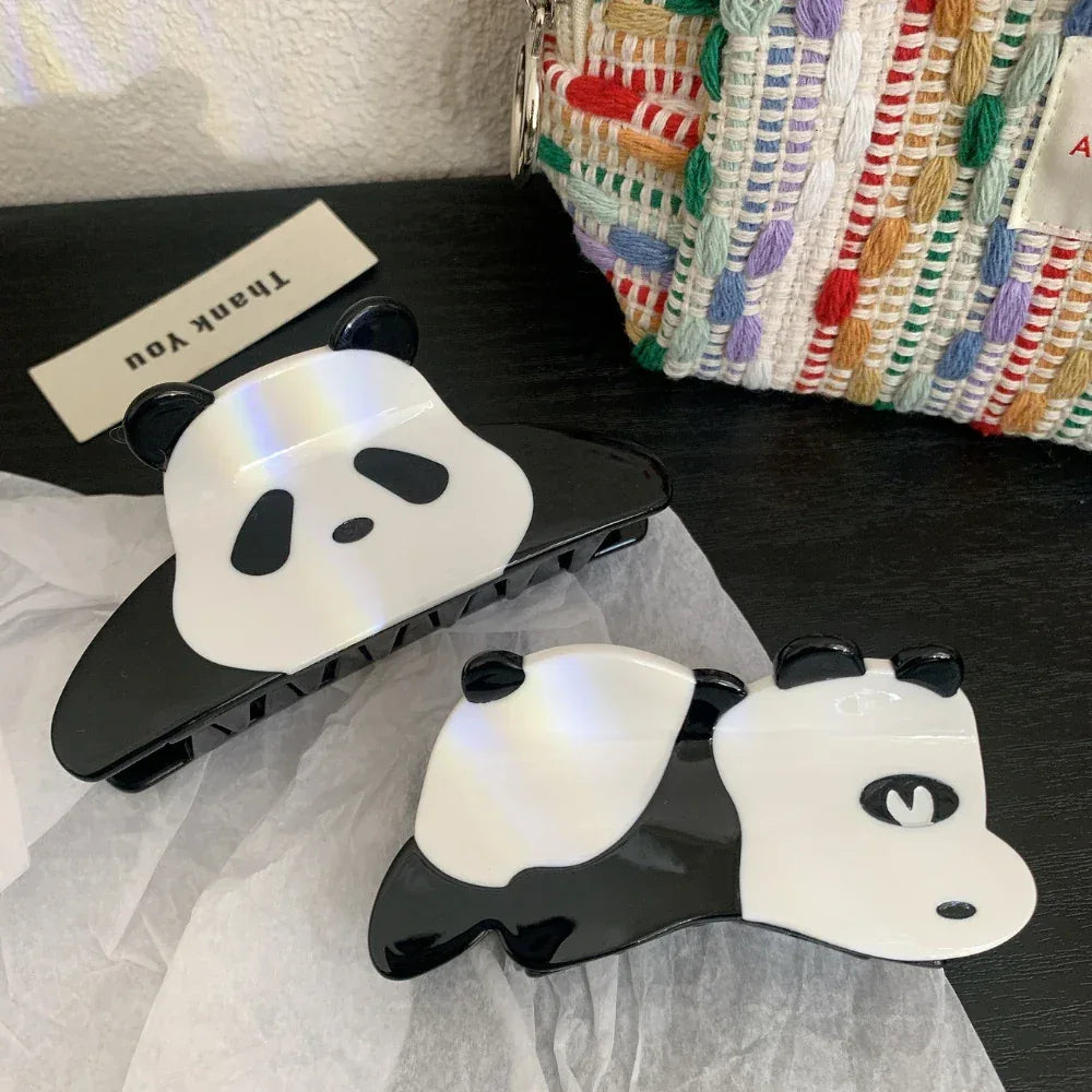 Two panda hair claw clips on a dark surface with a textured bag in the background