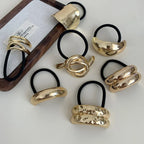 Various gold-tone abstract shape hair ties on a white surface and wooden tray