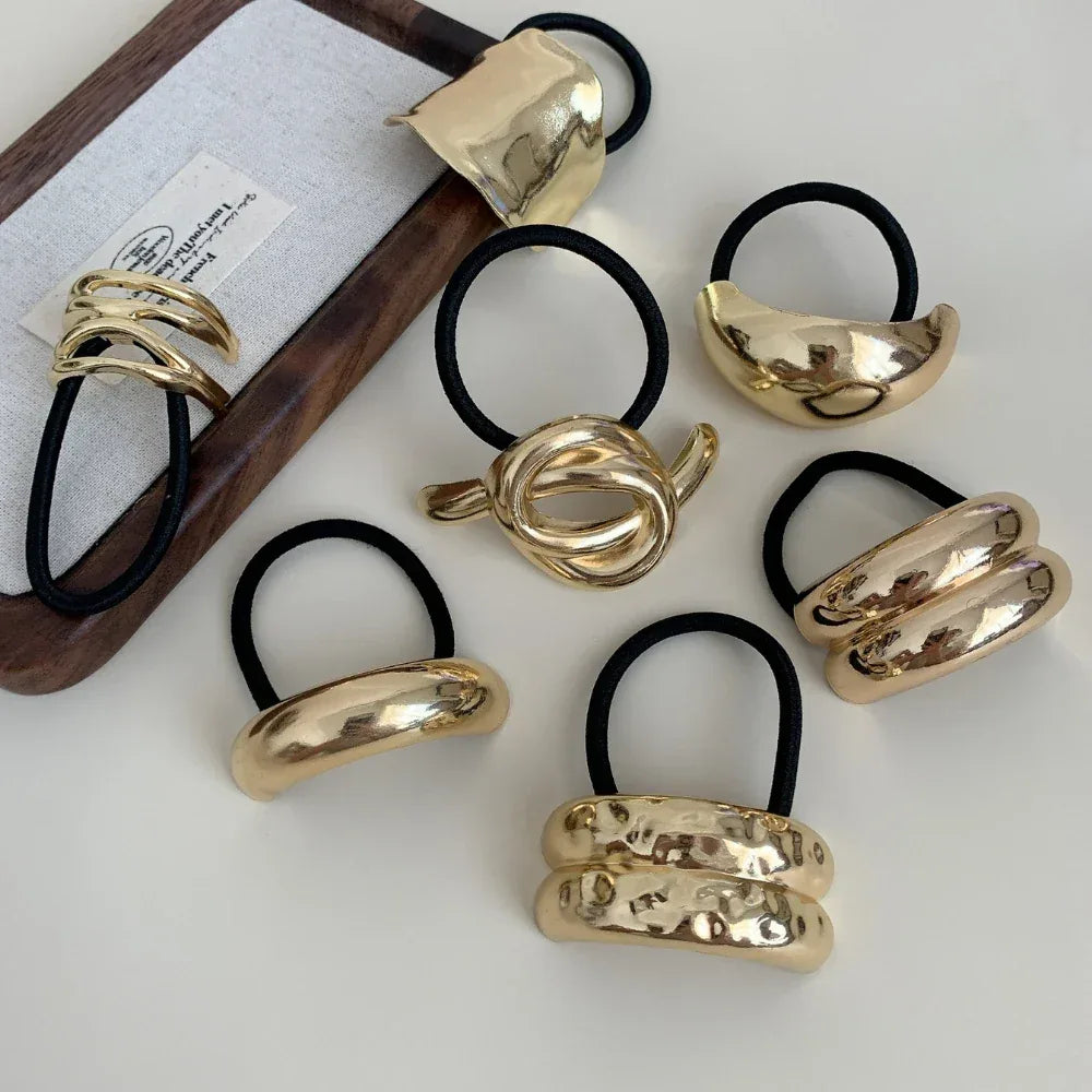 Various gold-tone abstract shape hair ties on a white surface and wooden tray