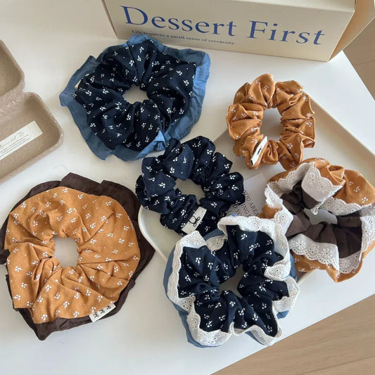 A collection of scrunchies with floral prints and ruffled edges are arranged on a white surface.
