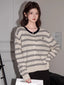 Woman wearing a cream and black striped button-up knit cardigan with a V-neck and embroidered detail.