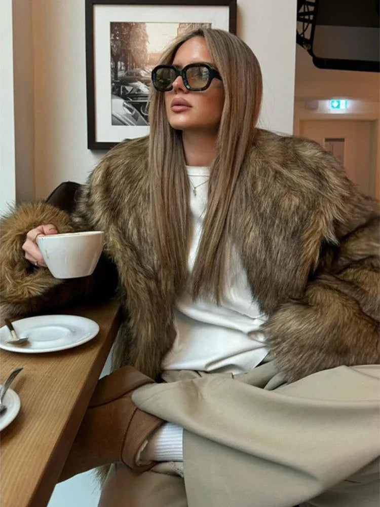 Close-up of a woman in a brown faux fur jacket and beige pants, holding a cup of coffee.