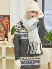 Close-up of a woman wearing a gray knit sweater dress with a Fair Isle pattern and a multi-colored fringed scarf.