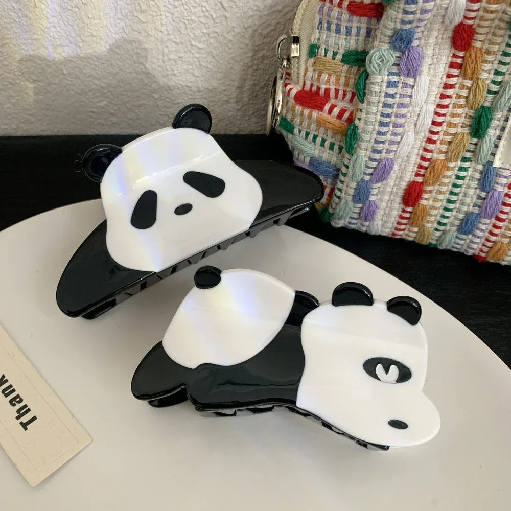 Two panda hair claw clips on a white surface with a textured bag in the background