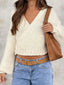 Woman wearing a cream chunky knit wrap sweater with light wash jeans and a brown belt, holding a brown tote bag.