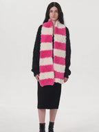 Model wearing a black sweater, black dress, and a pink and white striped fuzzy scarf.