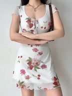 Woman wearing a white short-sleeve dress with a strawberry and rose print, featuring a tie-front neckline and a sheer hem.