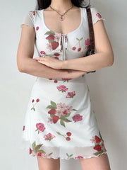 Woman wearing a white short-sleeve dress with a strawberry and rose print, featuring a tie-front neckline and a sheer hem.