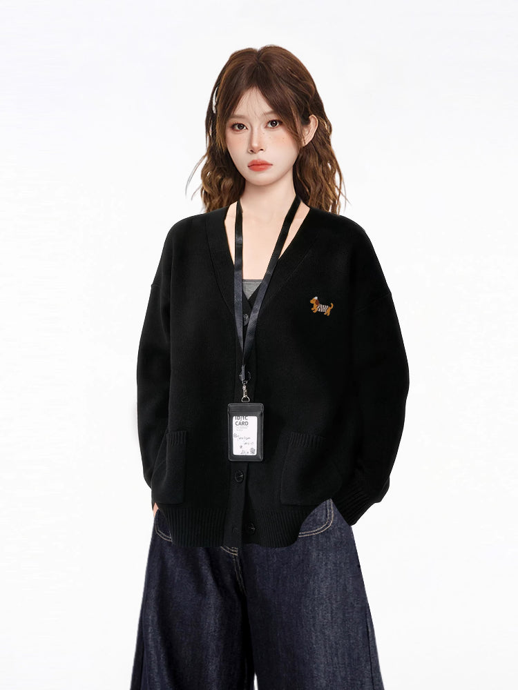 Model wearing a black V-neck knit cardigan with an embroidered dachshund detail, a black tank top, and dark wash wide-leg jeans, with an ID badge holder around her neck.