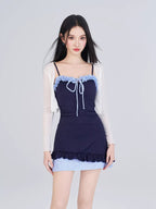 Model wearing a navy blue ribbed knit one-piece swimsuit with light blue gingham trim and a white sheer long-sleeved cardigan.