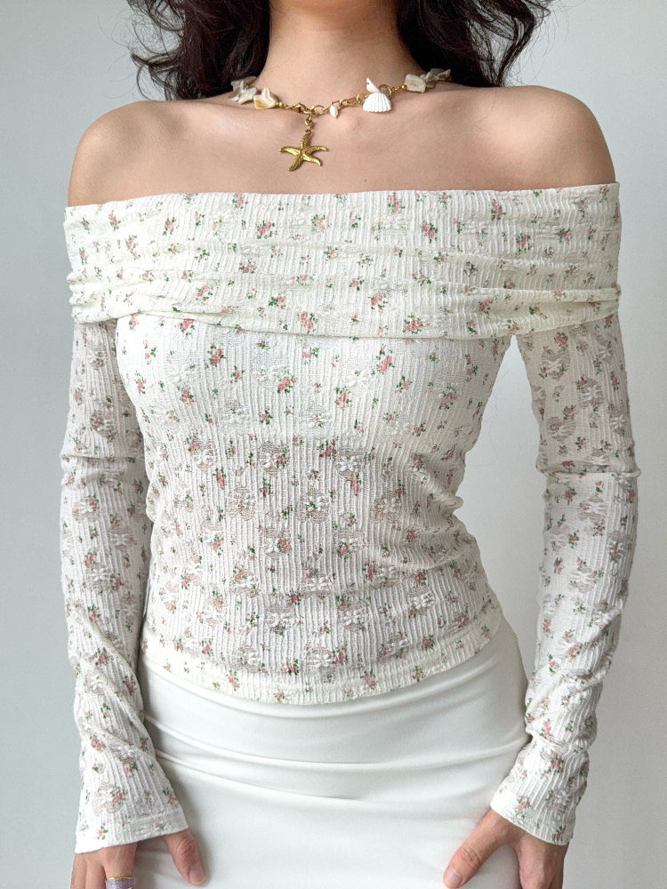 Woman wearing a white floral off-the-shoulder long-sleeved top paired with a white slip skirt and a seashell necklace.