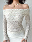 Woman wearing a white floral off-the-shoulder long-sleeved top paired with a white slip skirt and a seashell necklace.