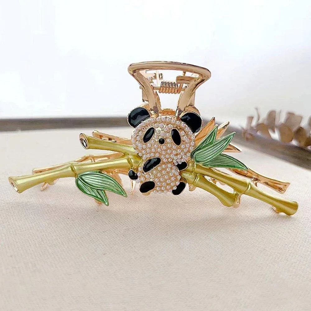 Close-up of a gold claw clip featuring a panda charm adorned with rhinestones, nestled on a bamboo branch with green enamel leaves.