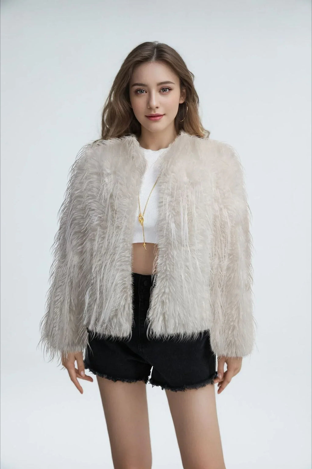 Model wearing a white faux fur jacket with a fringed texture, a cropped length, and an open front, paired with a white crop top and black shorts.