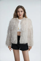 Model wearing a white faux fur jacket with a fringed texture, a cropped length, and an open front, paired with a white crop top and black shorts.