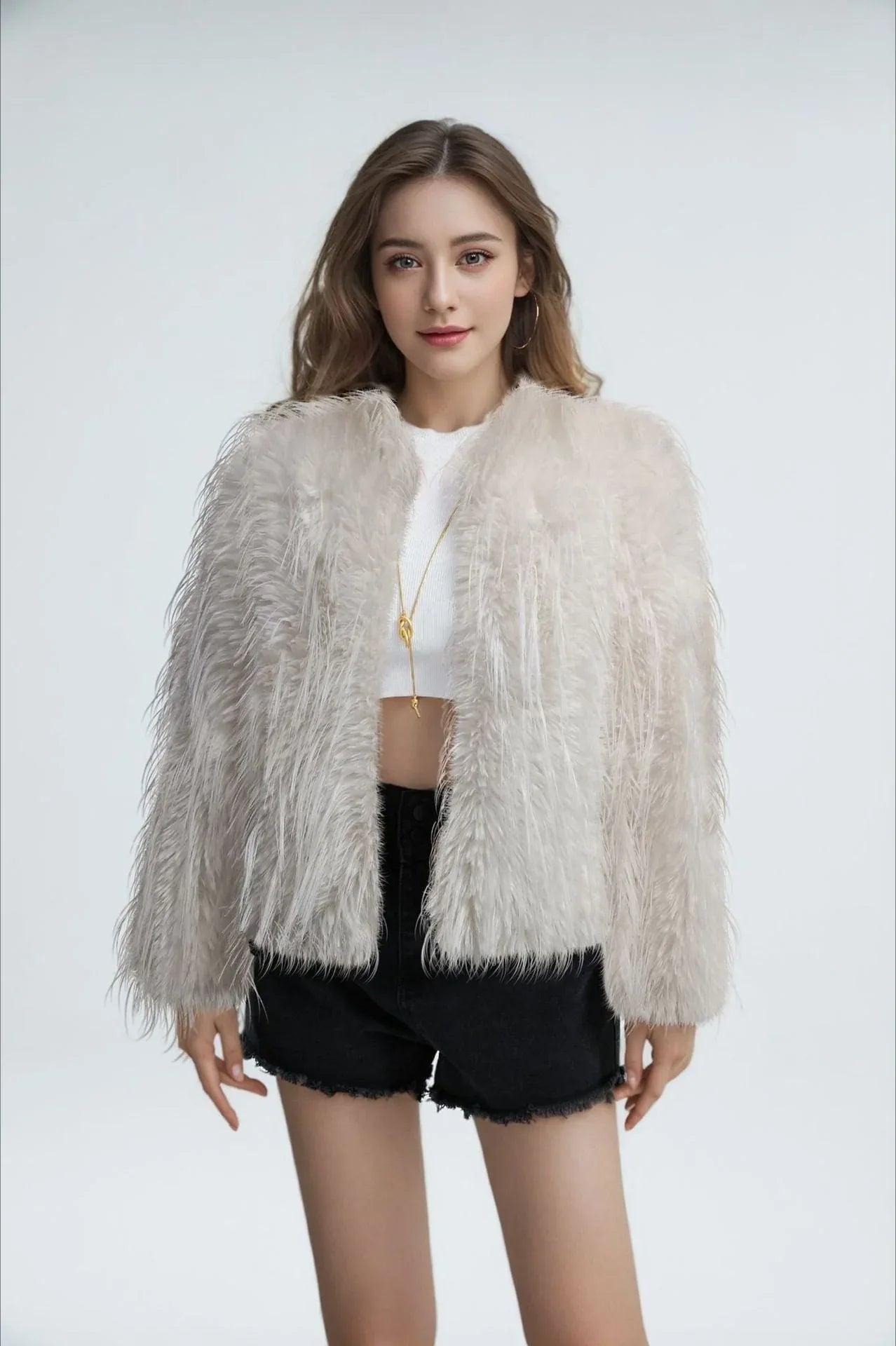 Model wearing a white faux fur jacket with a fringed texture, a cropped length, and an open front, paired with a white crop top and black shorts.