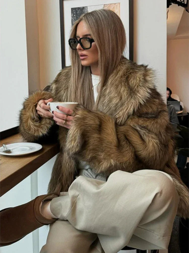 Woman wearing a brown faux fur jacket and beige pants, holding a cup of coffee. Main image