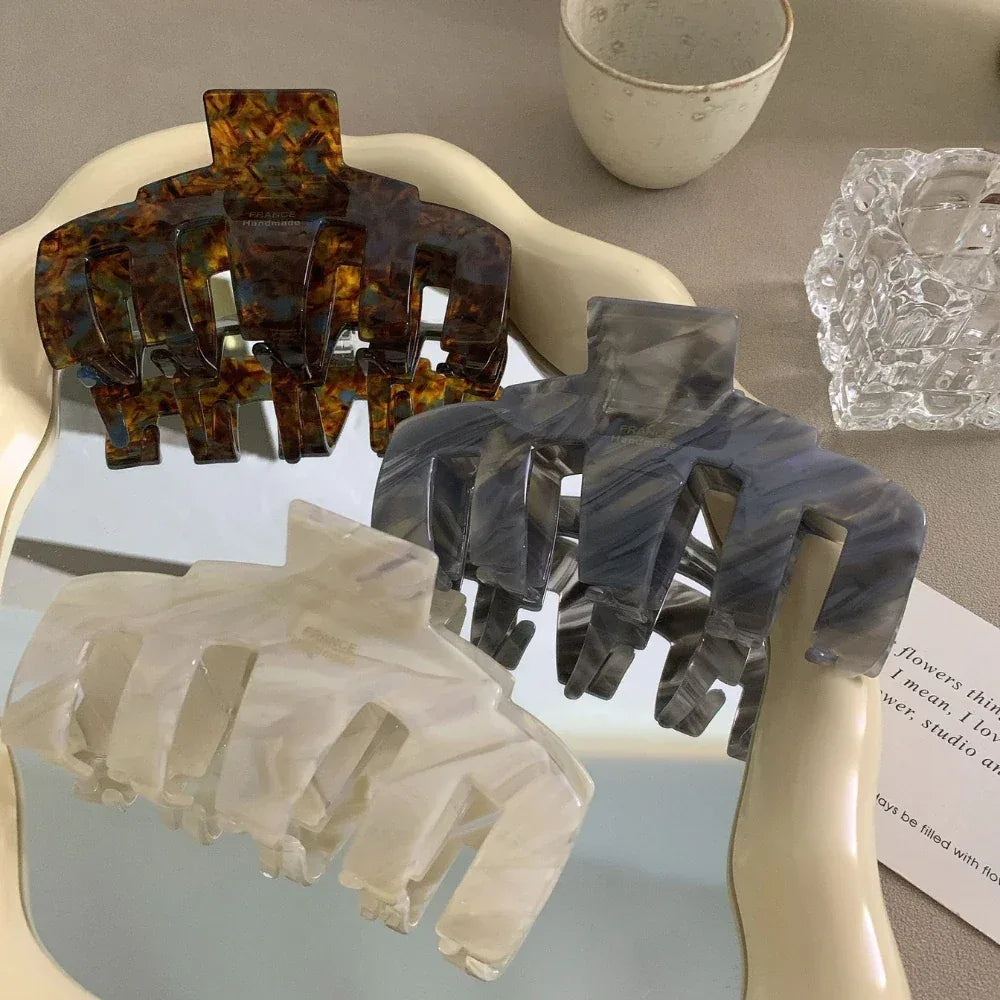 Three claw hair clips in tortoiseshell, grey, and white marbled patterns arranged on a mirrored surface.