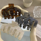 Three claw hair clips in tortoiseshell, grey, and white marbled patterns arranged on a mirrored surface.