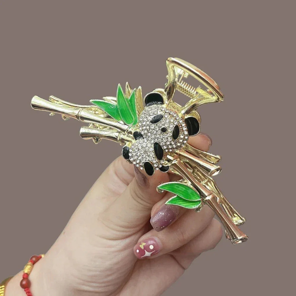 Side view of a gold claw clip with a detailed panda charm and bamboo branches, held by a hand.