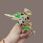 Side view of a gold claw clip with a detailed panda charm and bamboo branches, held by a hand.