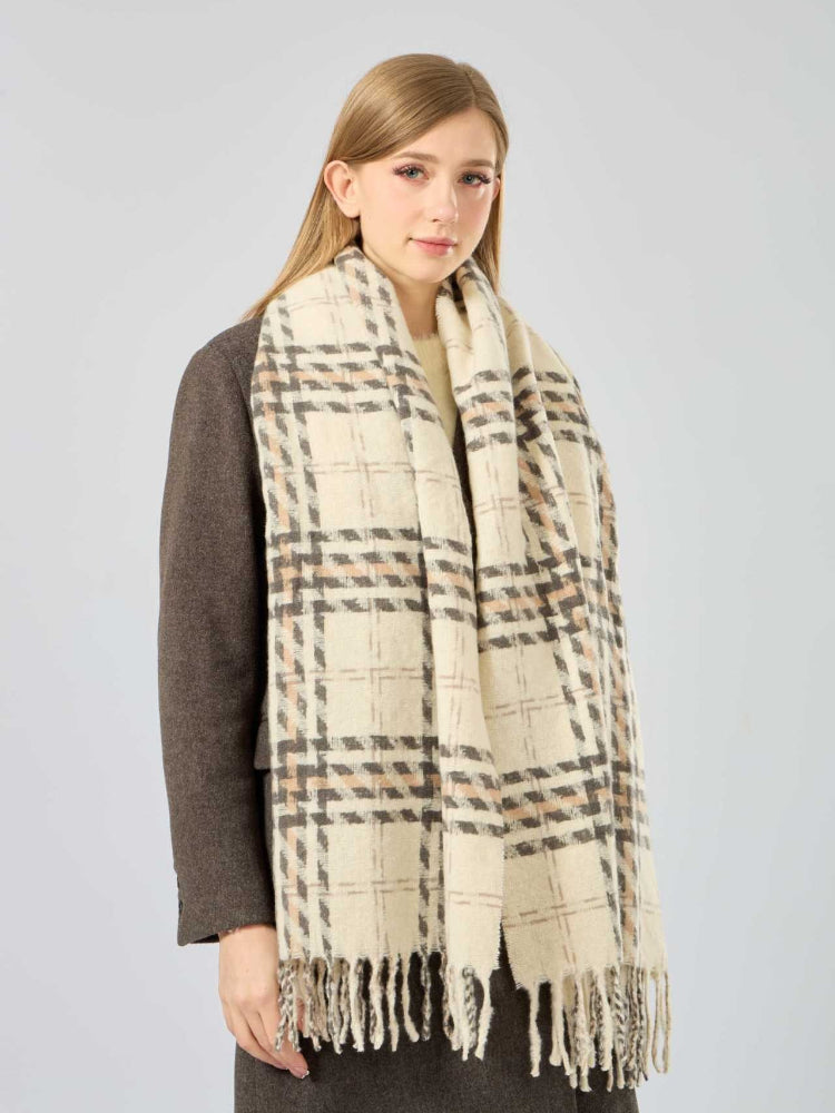 Full body shot of a woman wearing a brown coat and a cream, brown, and grey plaid scarf