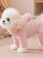 Fluffy white dog wearing a pink gingham dog coat with a hood and a pink pom-pom, attached to a leash.