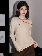 Woman wearing a cream off-the-shoulder long-sleeve top with red trim and brown pants, adjusting the neckline.