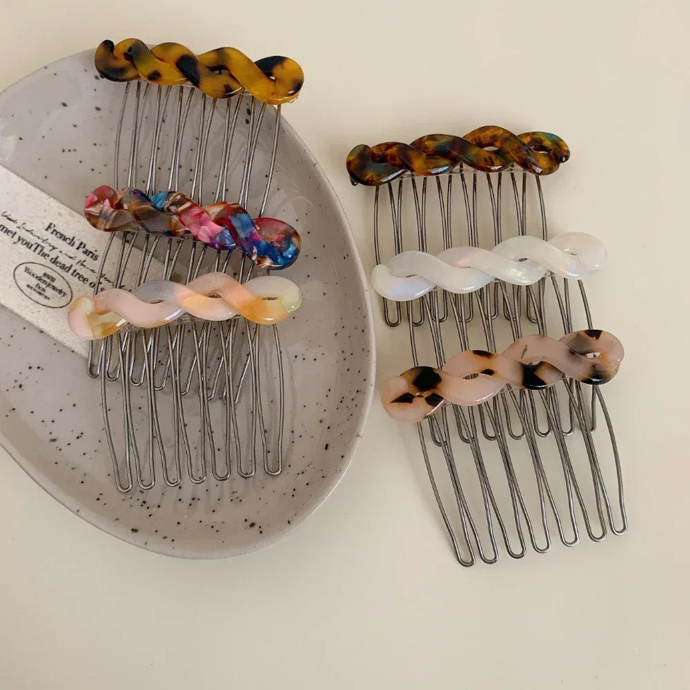 Assorted marbled resin twisted hair combs with metal teeth arranged on a grey oval dish