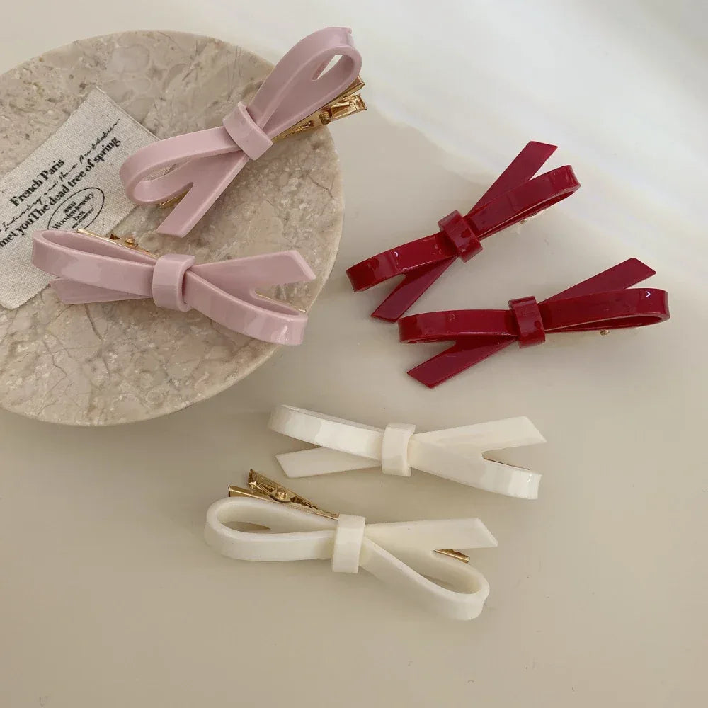 assorted resin bow barrettes in pink, red, and white displayed on a textured surface