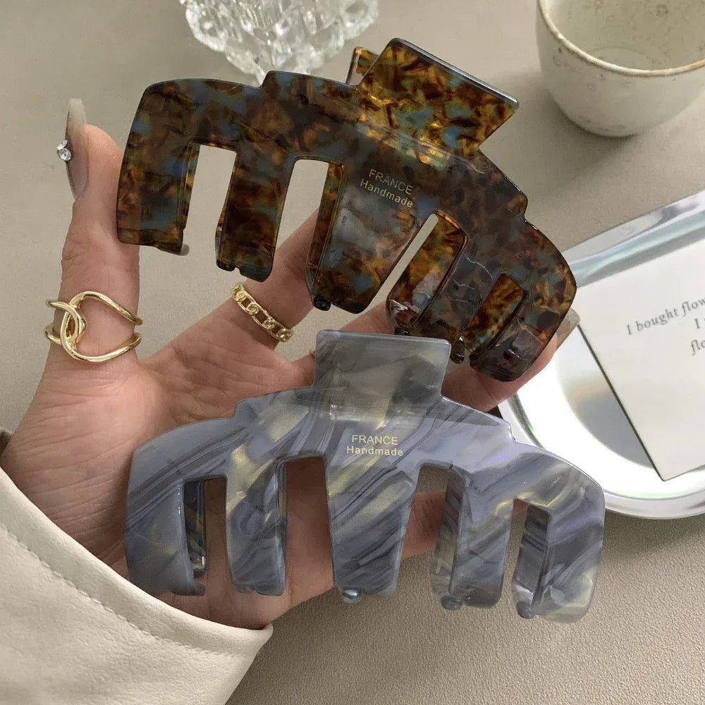 A hand holding two claw hair clips, one in tortoiseshell and one in grey marbled pattern.