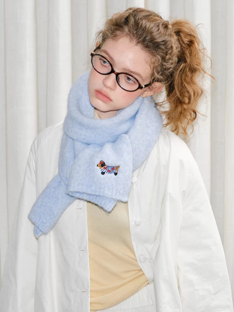 Side profile of a young woman wearing a light blue fuzzy knit scarf with an embroidered dog.