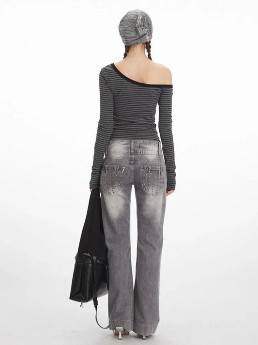 Back view of a woman wearing a grey and black striped off-the-shoulder long-sleeve top and grey wide-leg jeans with embellished back pockets.