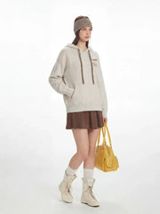 Model standing with one leg slightly forward, displaying the full casual outfit including the speckled knit hoodie, brown pleated skirt, white socks, cream lace-up boots, and yellow handbag.