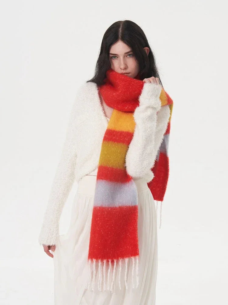 Woman wearing a white fuzzy sweater and a white pleated skirt, with a multi-colored striped scarf around her neck.