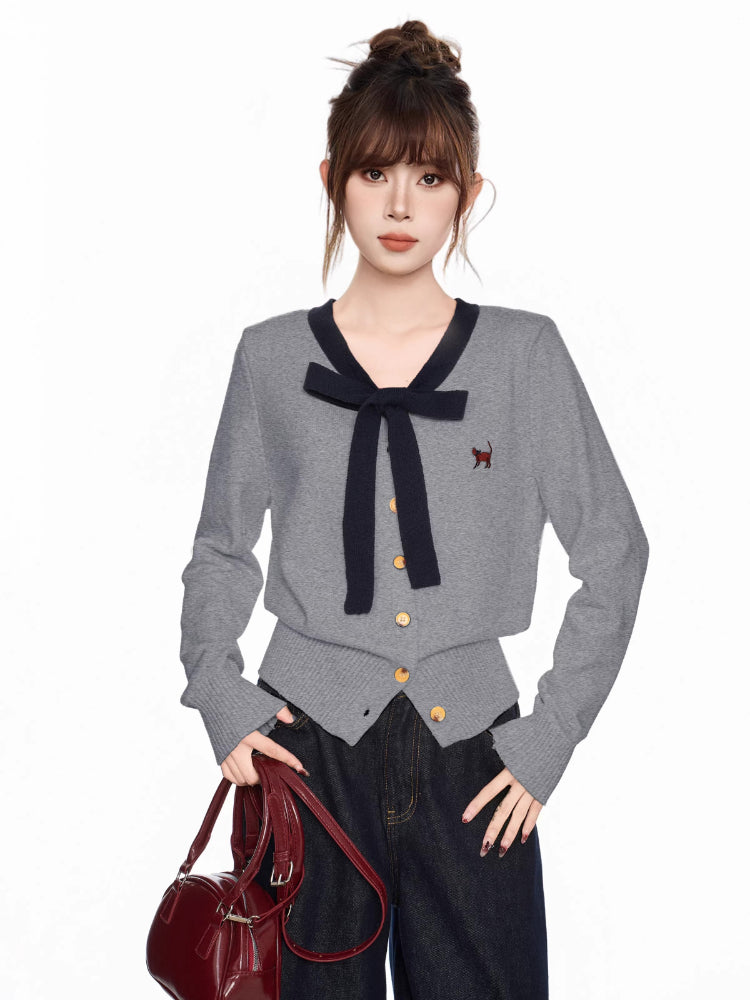 Woman wearing a grey cardigan with a navy bow and trim, dark wash wide-leg jeans, and a burgundy handbag.