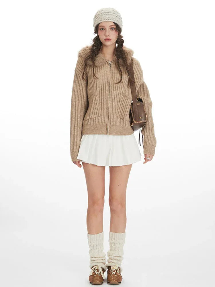 Model wearing a beige ribbed knit hooded jacket with faux fur trim, a white pleated mini skirt, white leg warmers, and a brown crossbody bag. Main image