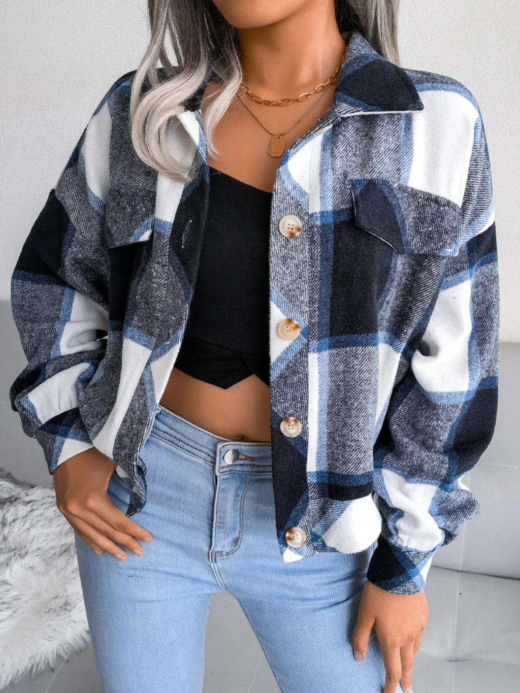 Woman wearing a blue, white, and black plaid flannel shirt jacket over a black crop top and light wash jeans, with hands in pockets.