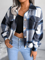 Woman wearing a blue, white, and black plaid flannel shirt jacket over a black crop top and light wash jeans, with hands in pockets.