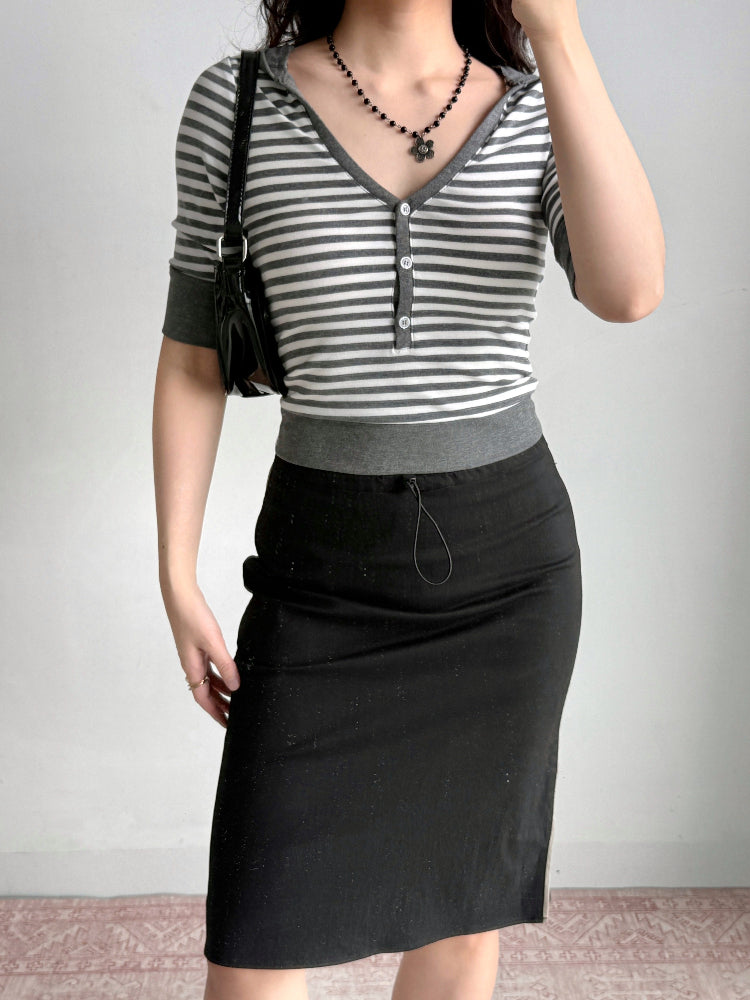 Full body shot of a woman wearing a grey and white striped cropped top, black skirt, and black handbag.