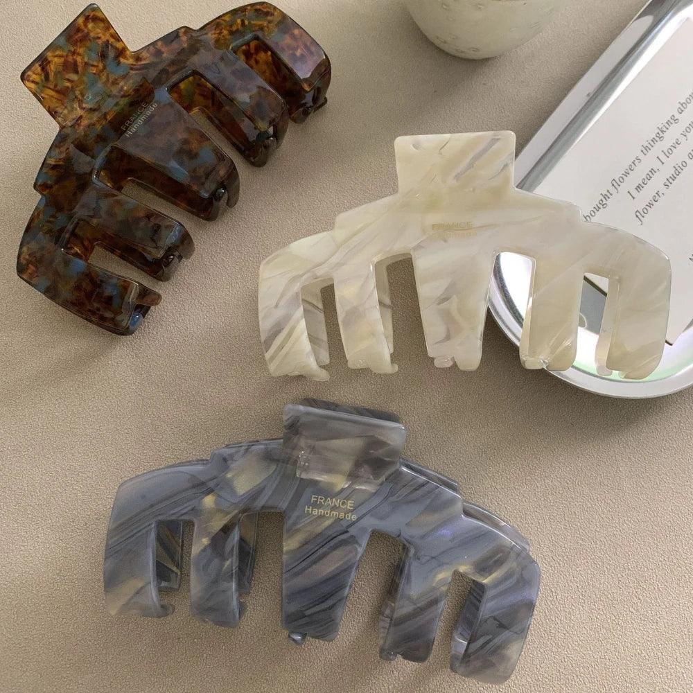 Four claw hair clips in tortoiseshell, grey, white marbled, and dark tortoiseshell patterns arranged on a flat surface.