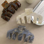 Four claw hair clips in tortoiseshell, grey, white marbled, and dark tortoiseshell patterns arranged on a flat surface.