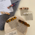 Various marbled resin twisted hair combs with metal teeth displayed on a grey scarf and a marble coaster