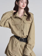 Close-up of a woman's torso wearing a tan button-down shirt dress with a black studded belt.
