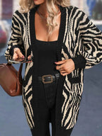 Close-up of a woman wearing a black and white zebra print longline knit cardigan, holding a smartphone and a brown handbag.
