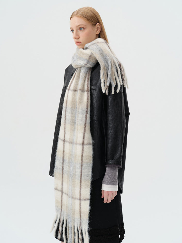 Side view of a model wearing a black jacket, grey top, and a long blue and beige plaid scarf with fringe