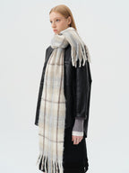 Side view of a model wearing a black jacket, grey top, and a long blue and beige plaid scarf with fringe