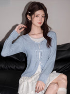 A woman models a light blue knit cardigan layered over a white camisole and a ruffled skirt.